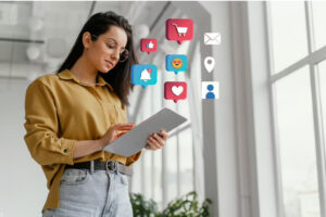 Como construir um brand safety para sua marca no mobile 2 Mulher mexendo em tablet enquanto ícones relacionados à redes sociais são projetados para fora da tela.