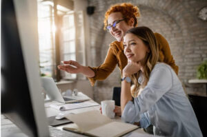 Duas profissionais de marketing felizes com os dados apresentados na tela do computador.